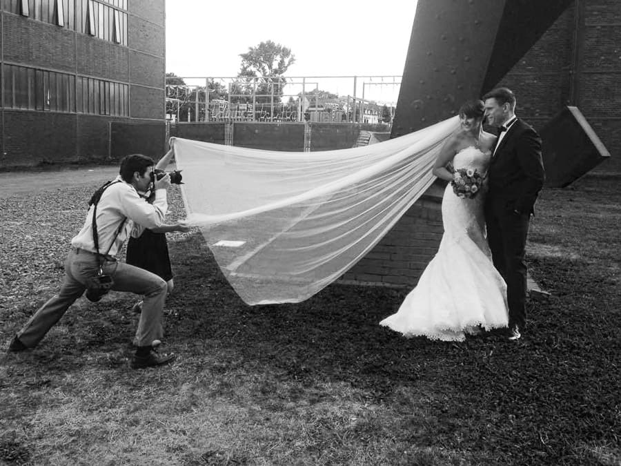 Hochzeitsfotograf Vladimir Dimitrov macht Bilder vom Brautpaar. Mädchen hält den Schleier für eine interessante Perspektive.
