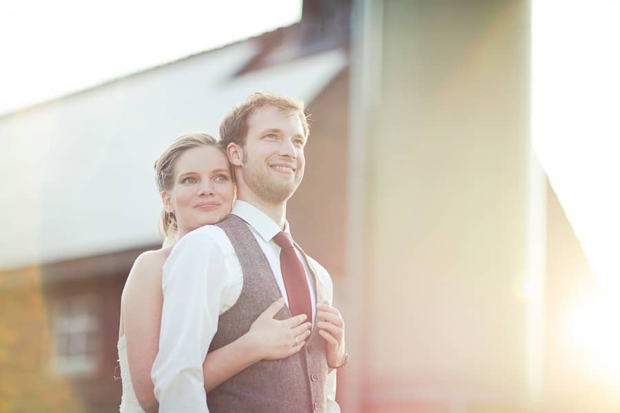 Braut umarmt Bräutigam von hinten beide lächeln, erstrahlt vom Licht mit tollen Lichteffekten durch Gegenlicht