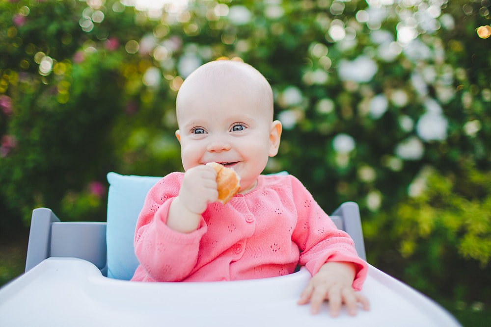 Zuckersüßes Baby im Garten mit Brötchen lächelt in der Hand 