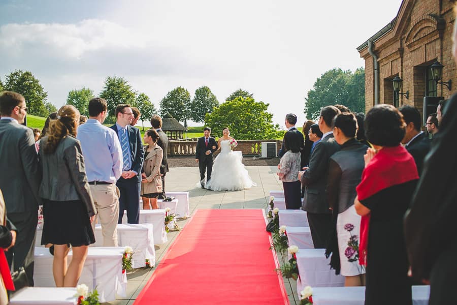 Bei der freien Trauung auf der Terrasse vom Kosaido in Düsseldorf wird die Braut von ihrem Vater über einen roten Teppich zum Bräutigam geführt