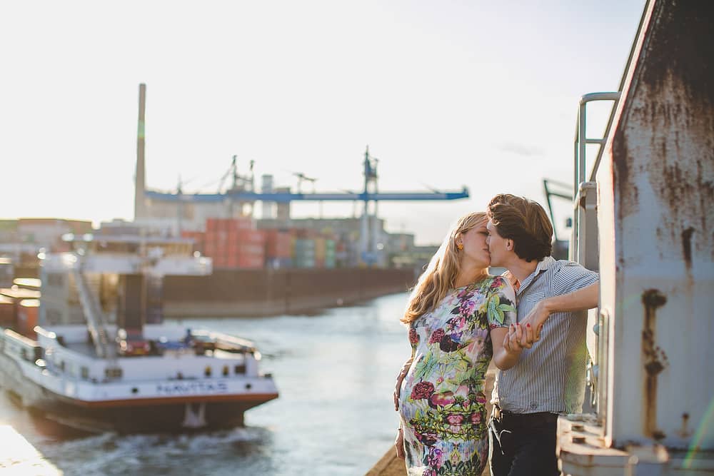 Schwangere mit Babybauch küsst ihren Partner am Industrie Hafen in Düsseldorf. Ein Schiff nähr sich. Industrie Kulissen.